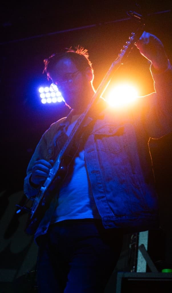 Guitarist playing electric guitar under warm and blue stage lighting
