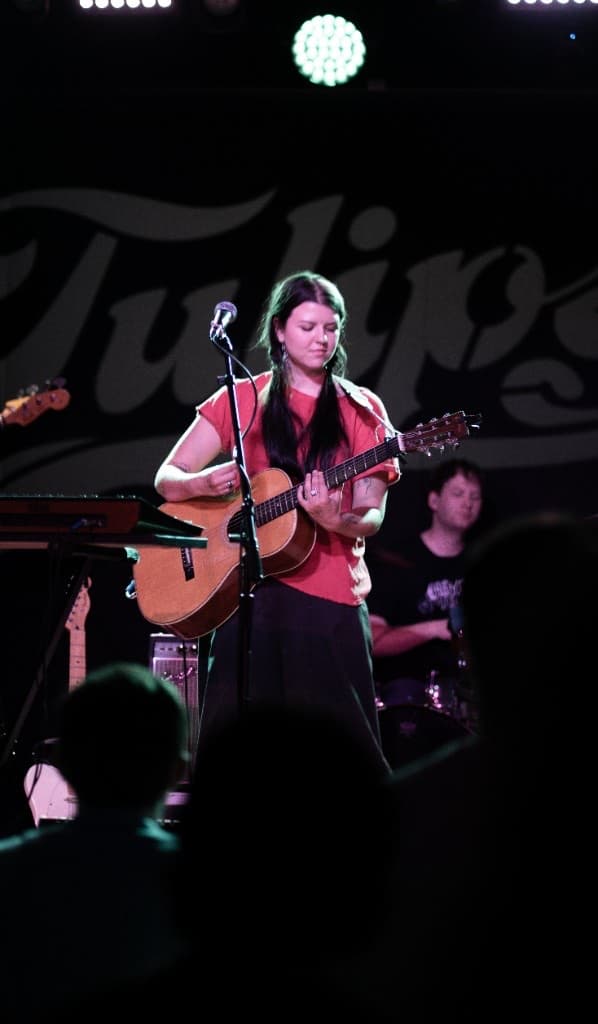 Musician singing and playing acoustic guitar on a lit stage