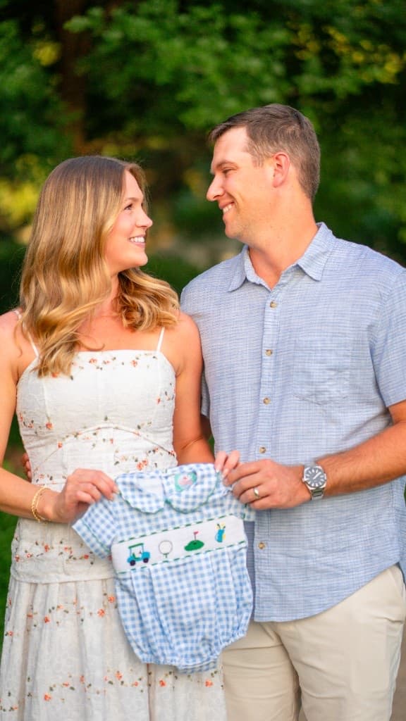 Expectant couple in a park with ultrasound images draped over the man's shoulder