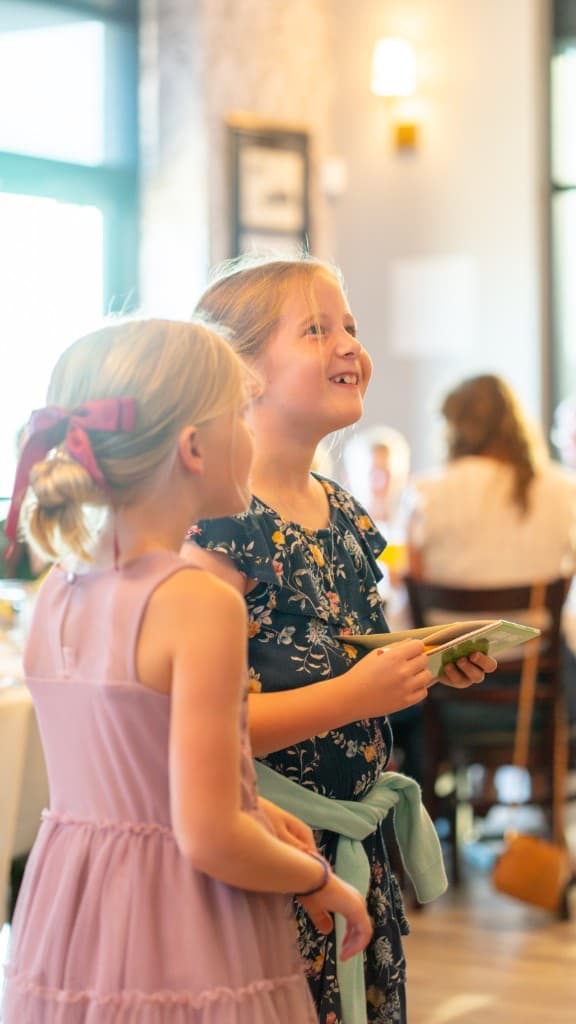 Two young girls smiling in a sunlit dining room