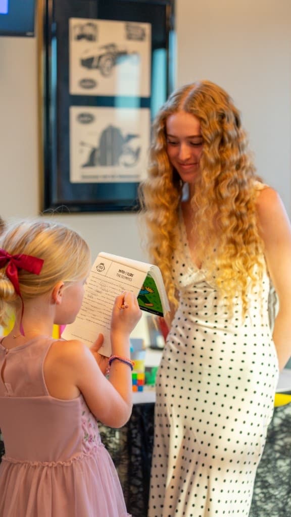 Young girl writing in a book while a teenager looks on and smiles